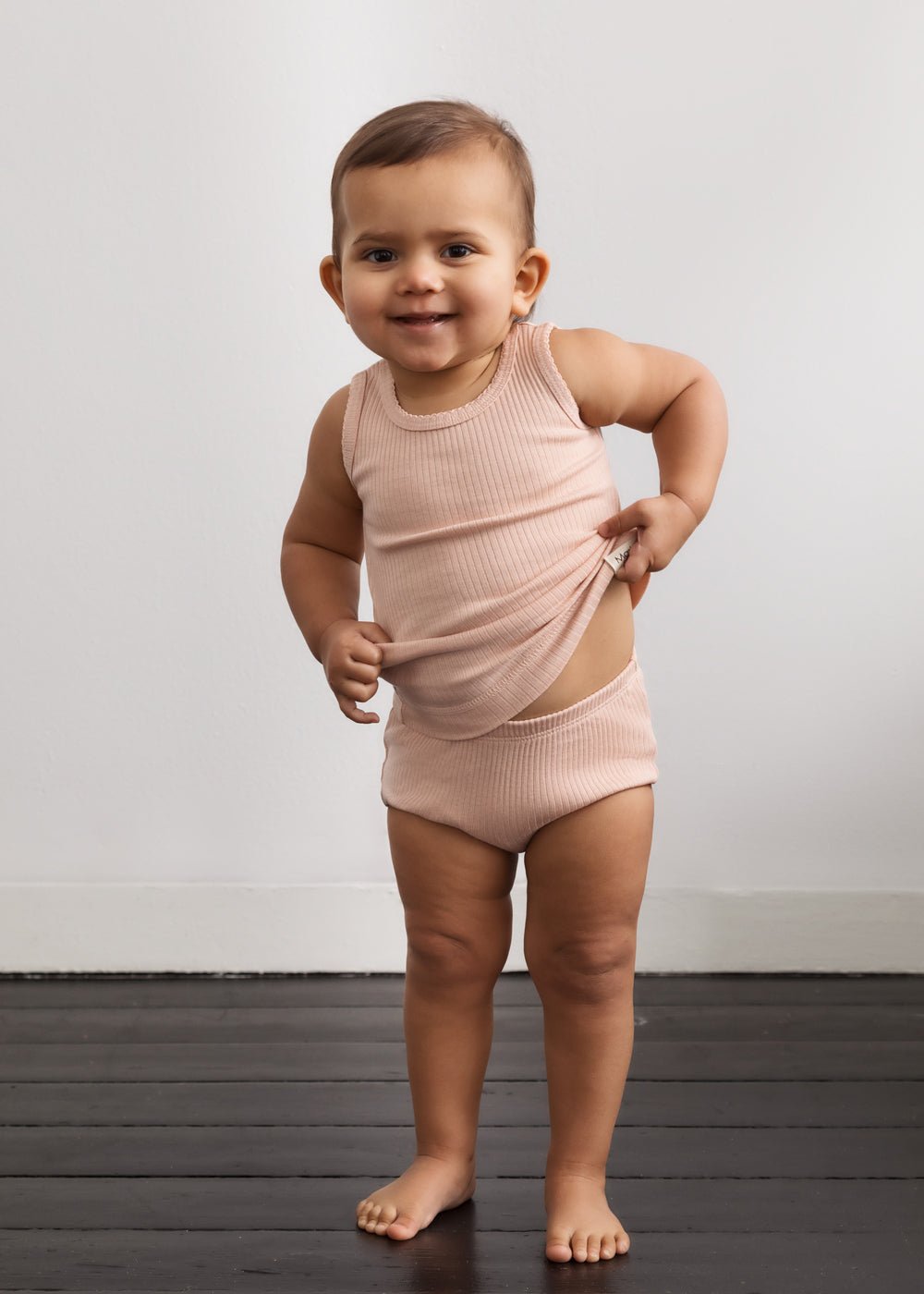 Baby-ærmeløs undertrøje i lys rosé på model, ribstrik med rund hals