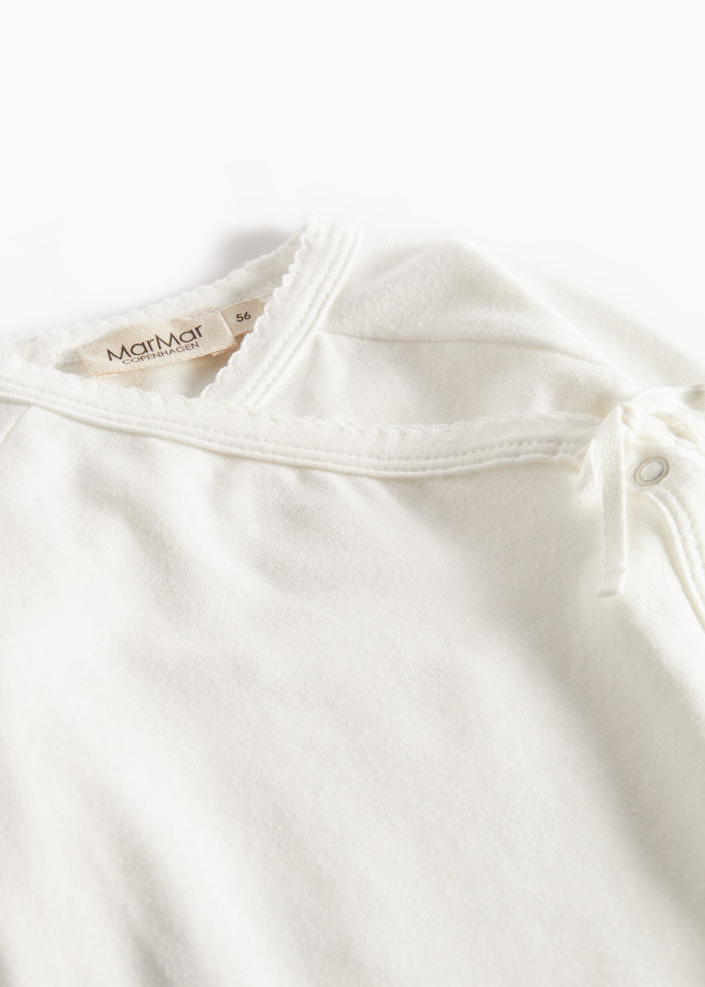 Hvid babybluse med rund hals og dekorative knapper ved skulderen