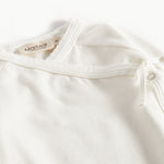 Hvid babybluse med rund hals og dekorative knapper ved skulderen