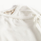Hvid babybluse med rund hals og dekorative knapper ved skulderen