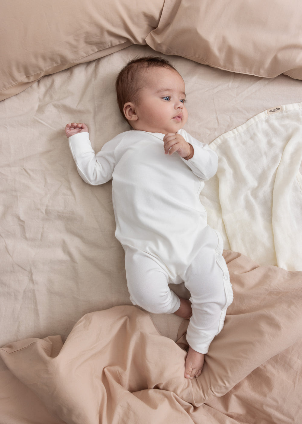 Baby iført beige/grå strikket sæt liggende i flettet kurv med beige tæppe