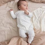 Baby iført beige/grå strikket sæt liggende i flettet kurv med beige tæppe