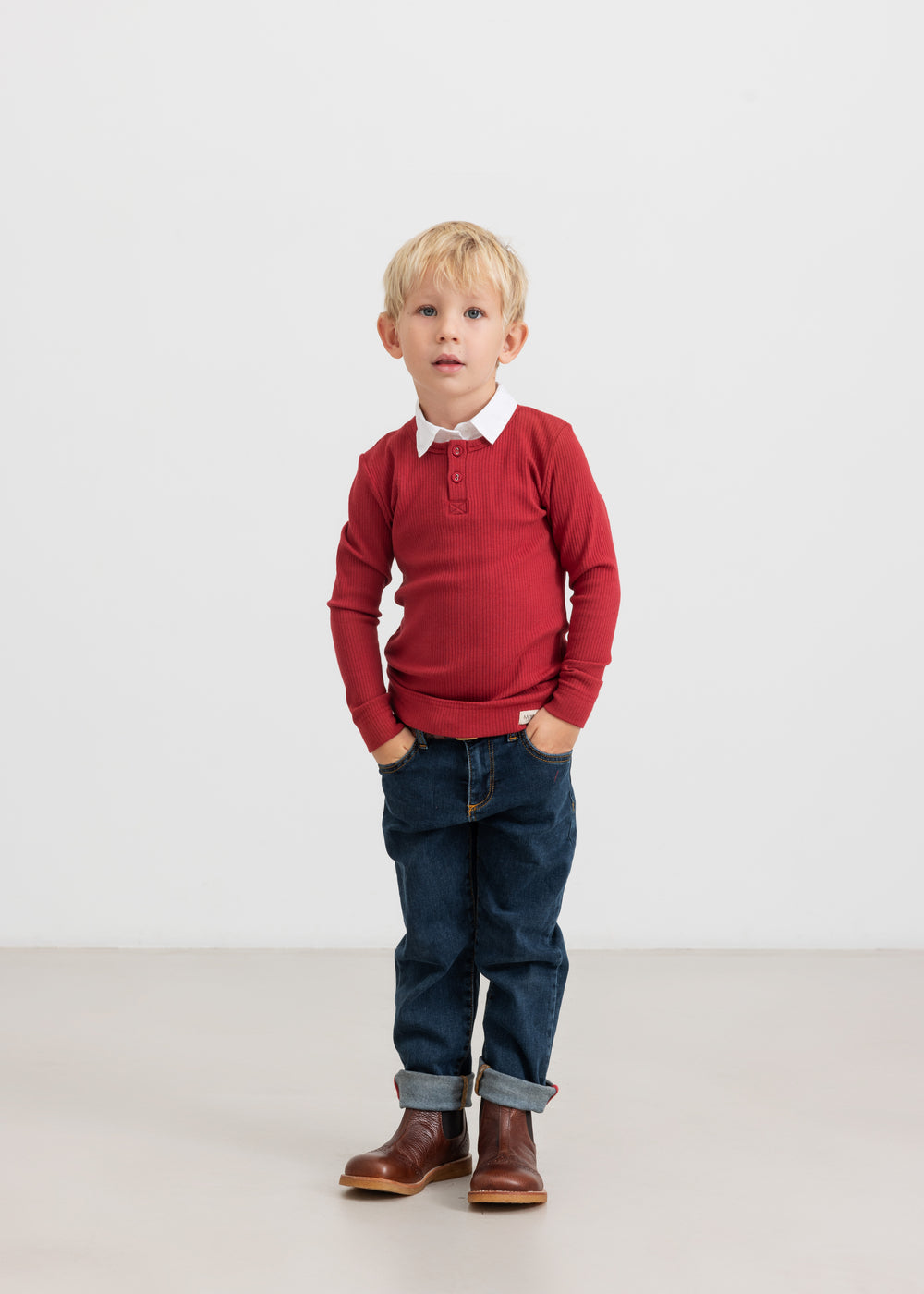 Dreng iført rød ribbluse, hvid skjorte og mørke børnejeans.