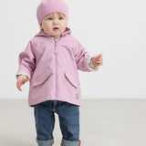 Baby iført lyserød overgangsjakke, rosa hue og jeans