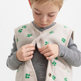 Barn iført beige vest med grønt kløverprint lukket foran