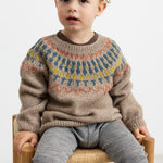 Dreng iført beige uldstrikbluse med mønster sidder på stol.