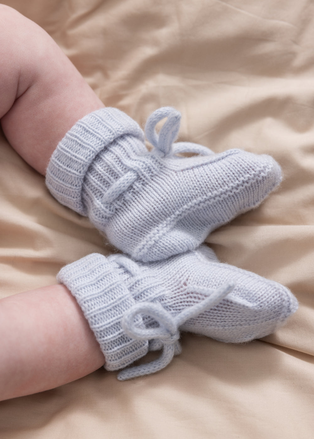 Strikkede lyseblå babysutsko på model med bundne snørebånd