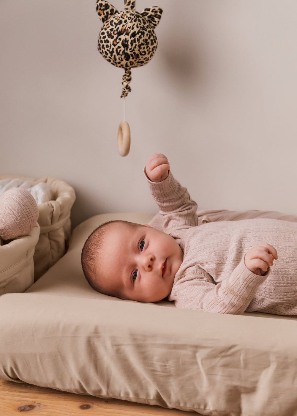 Sandfarvet skiftepudebetræk med glat stof, på liggeunderlag under baby.