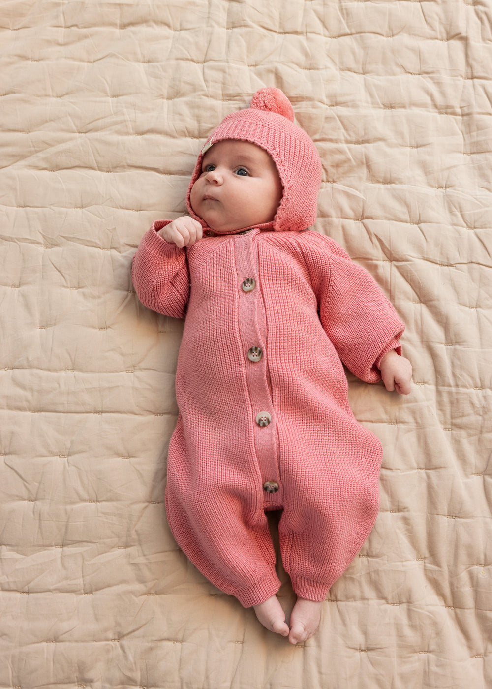 Lyserød strikhue i strik med pompon på baby i rosa heldragt