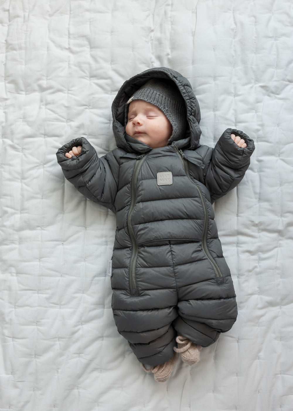 Baby ligger på tæppe iført mørkegrå dundragt.