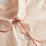 Detalje af beige pyjamas: ståkrave med orange kant og knaplukning ved halsen