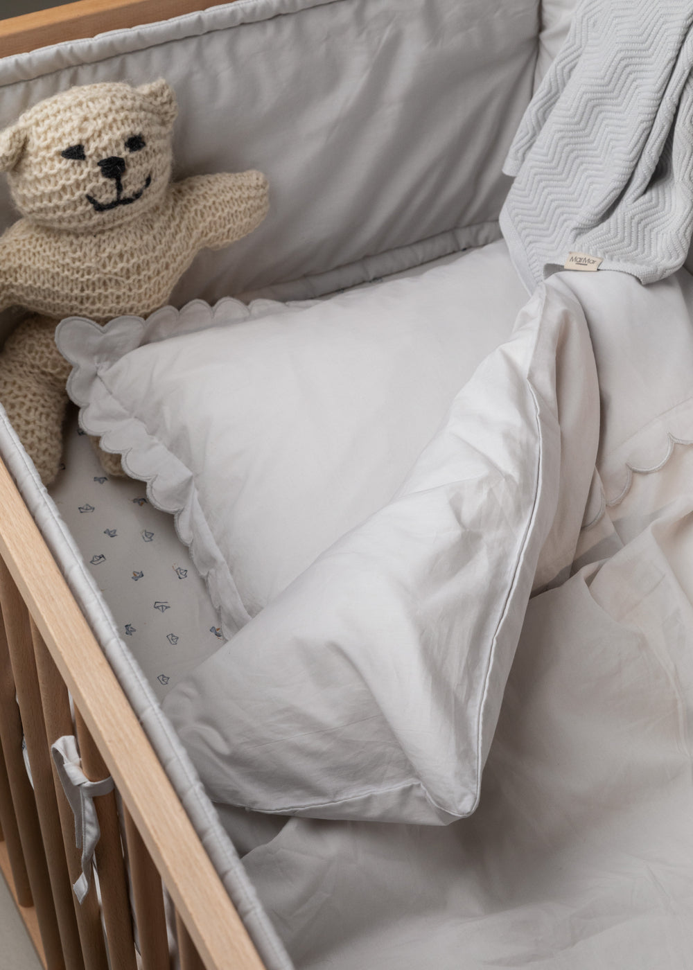 Hvidt babysengetøj i krybbe med pude, dyne og skalkantet kant.