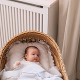 Babysengetøj i hvidt med skalkant; baby ligger i kurv med dyne og pude.