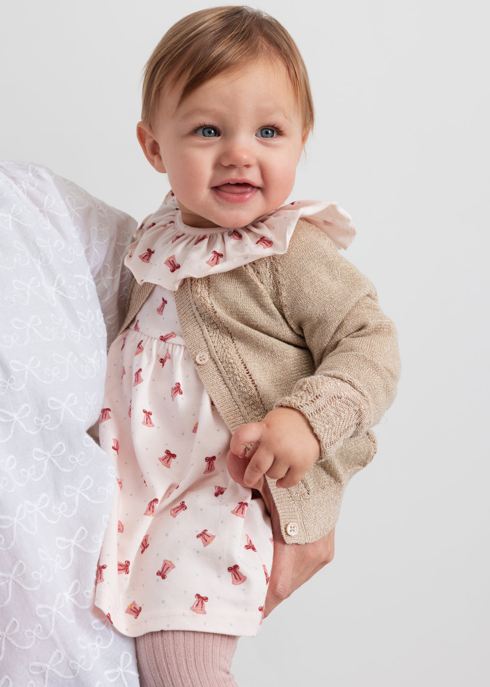 Baby iført kjole med røde juleklokker og cremefarvet cardigan