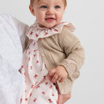 Baby iført kjole med røde juleklokker og cremefarvet cardigan