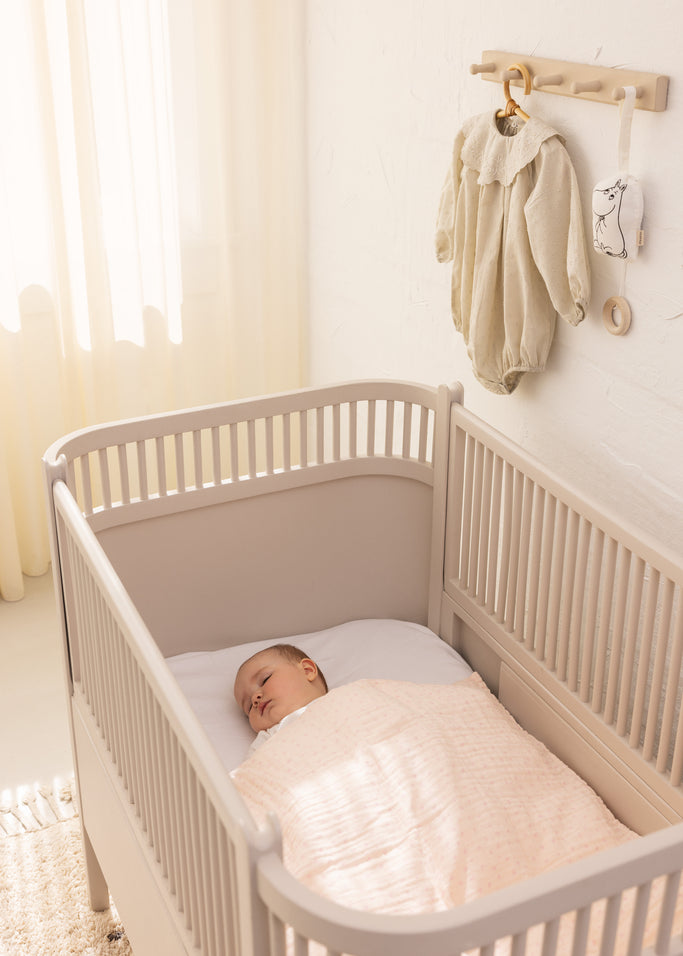 Musikuro til babyseng med hængende stofdele og rund ring ved tremmeseng