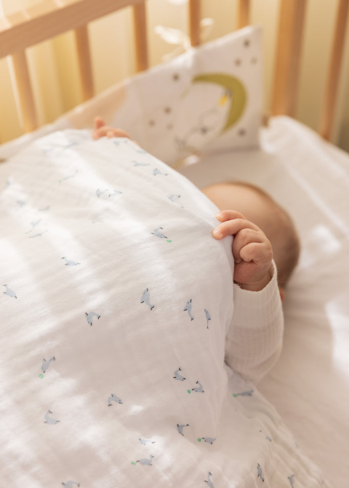 Babysengetøj i hvidt med små delfinprint i blå og grønne nuancer