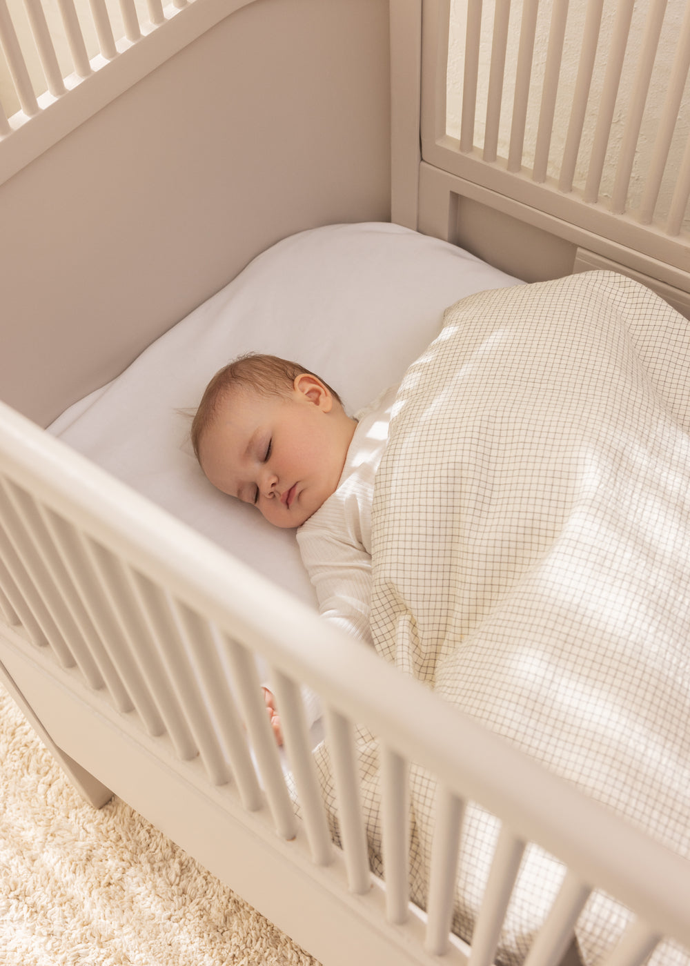 Babysengetøj i cremefarvet tern i vugge med sovende baby
