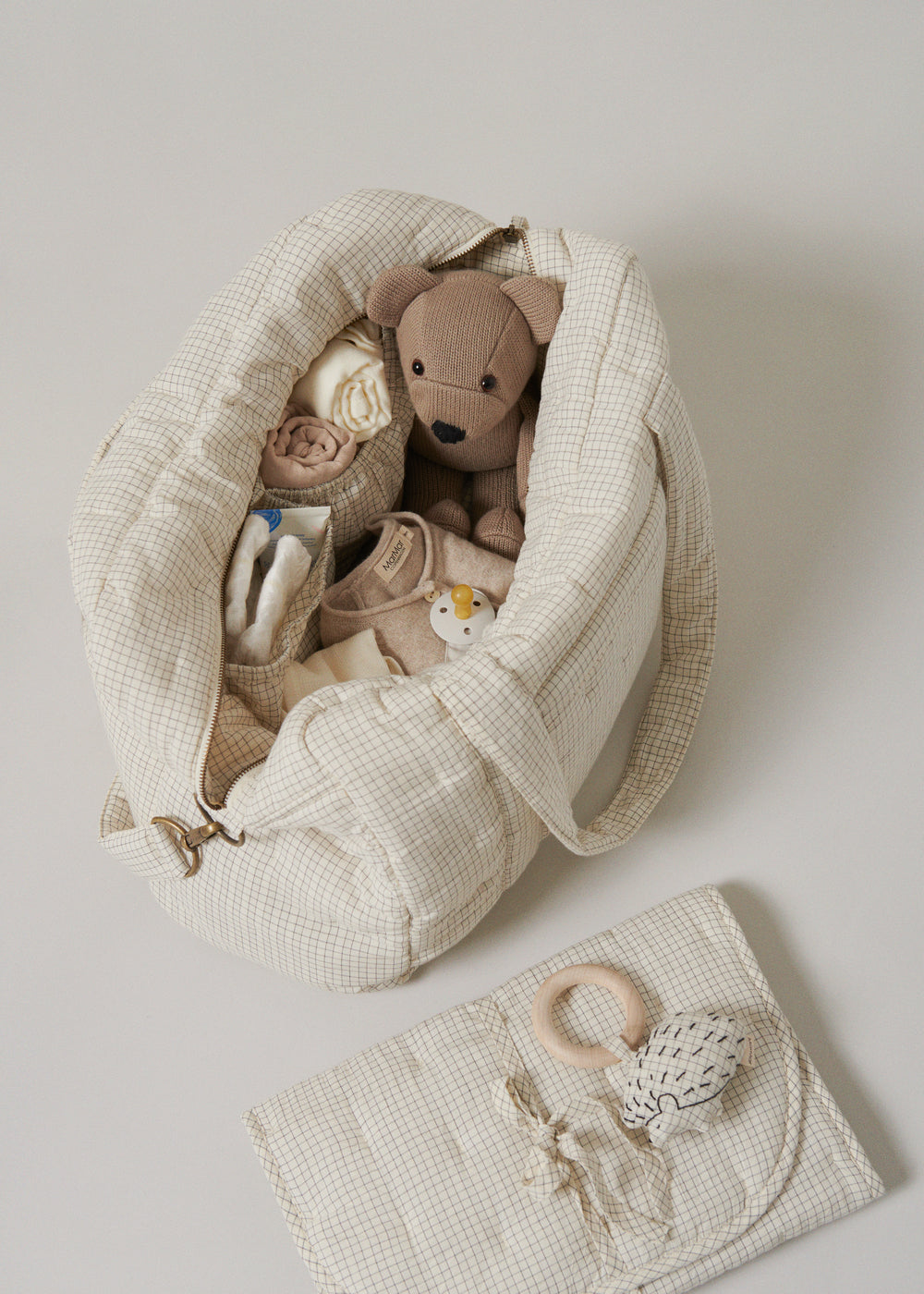 Åbnet ternet pusletaske i beige med opbevaring til baby, sut og legetøj indeni