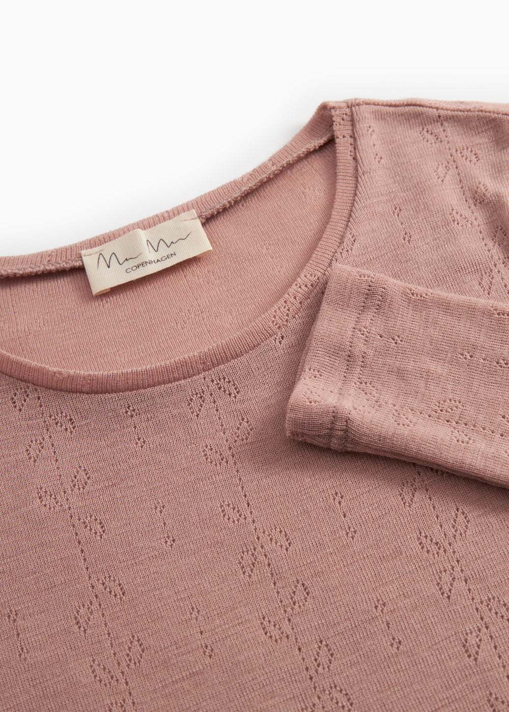 Detalje af rosenrosa uld-pointelle t-shirt: rund hals, hulmønster og blød rib