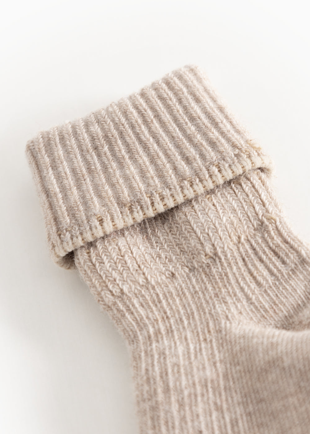 Nærbillede af babystrømpe i lyse beige melé med ribkant ved overkanten