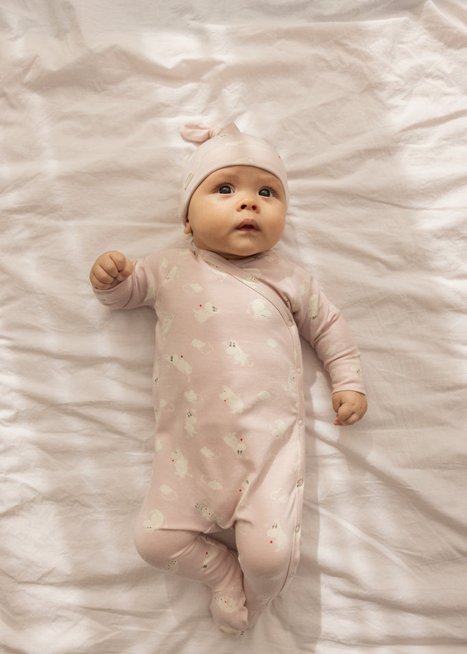 Rosa babyheldragt med lange ærmer og ben, samlet trykknaplukning og små Moomin-figurer
