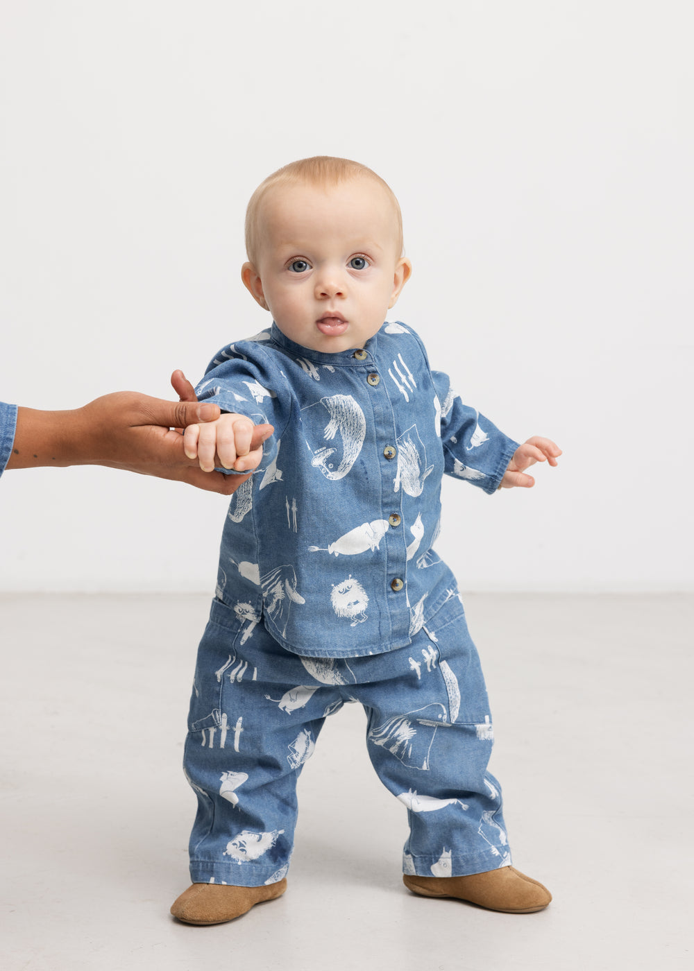 Blå baby-skjorte i denim med knaplukning og Moomins-mønster på barnet.