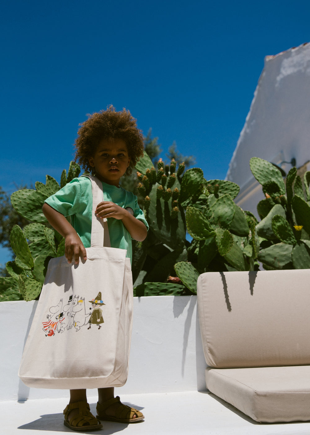 Creme shopper-taske med Moomin-figurer foran, bæres i hånden