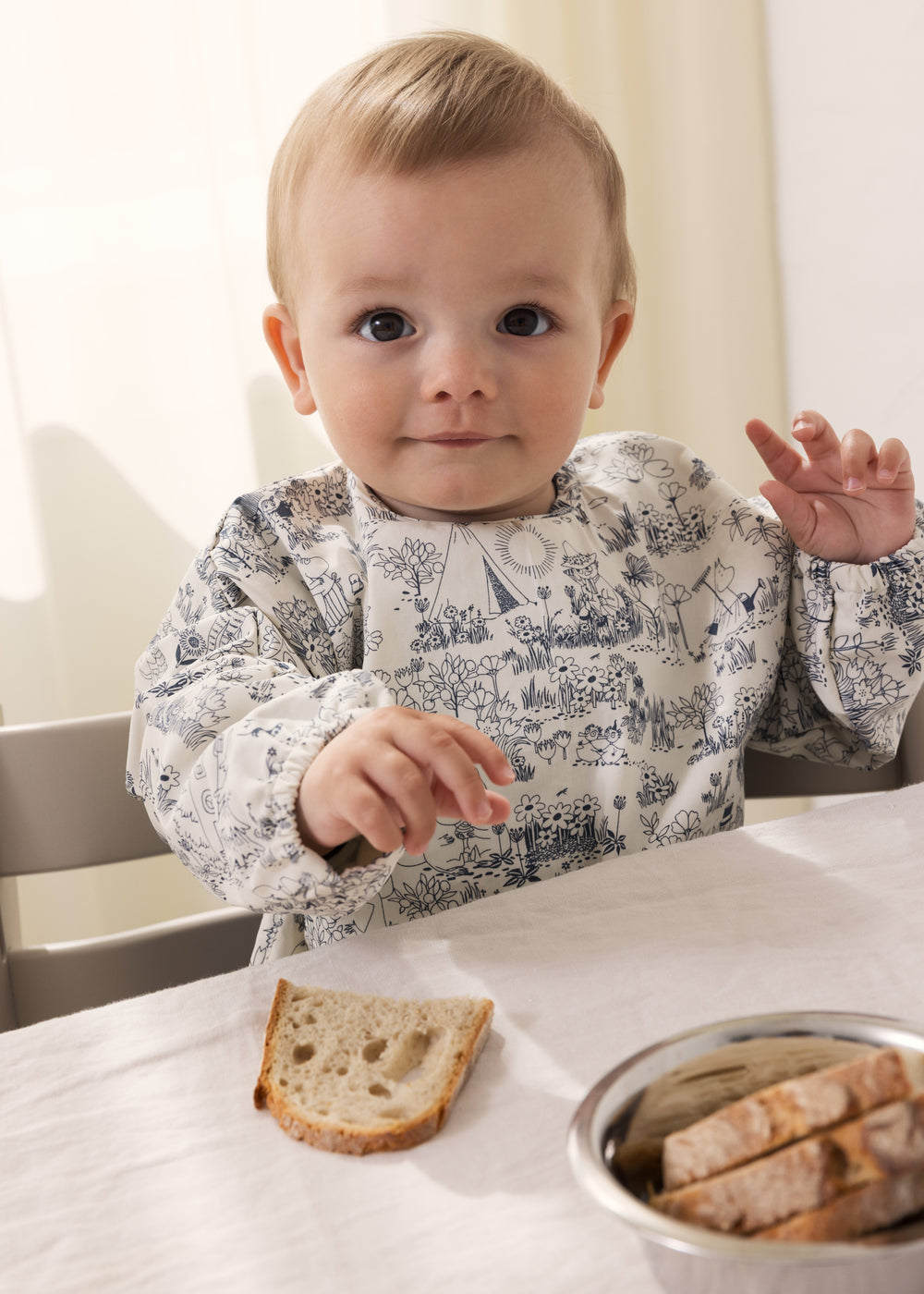 Langærmet spiseforklæde i hvidt og blåtgråt med Mumin-motiv, påklædt til baby