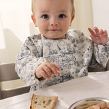 Langærmet spiseforklæde i hvidt og blåtgråt med Mumin-motiv, påklædt til baby
