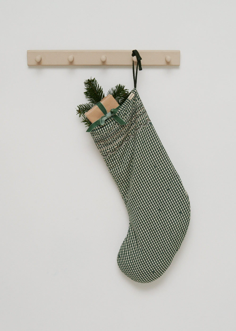 Grønternet julesok på vægkrog med pinegren og lille beige pynt i toppen