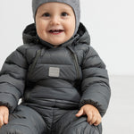 Smilende baby i mørkegrå dundragt sidder på gulv.