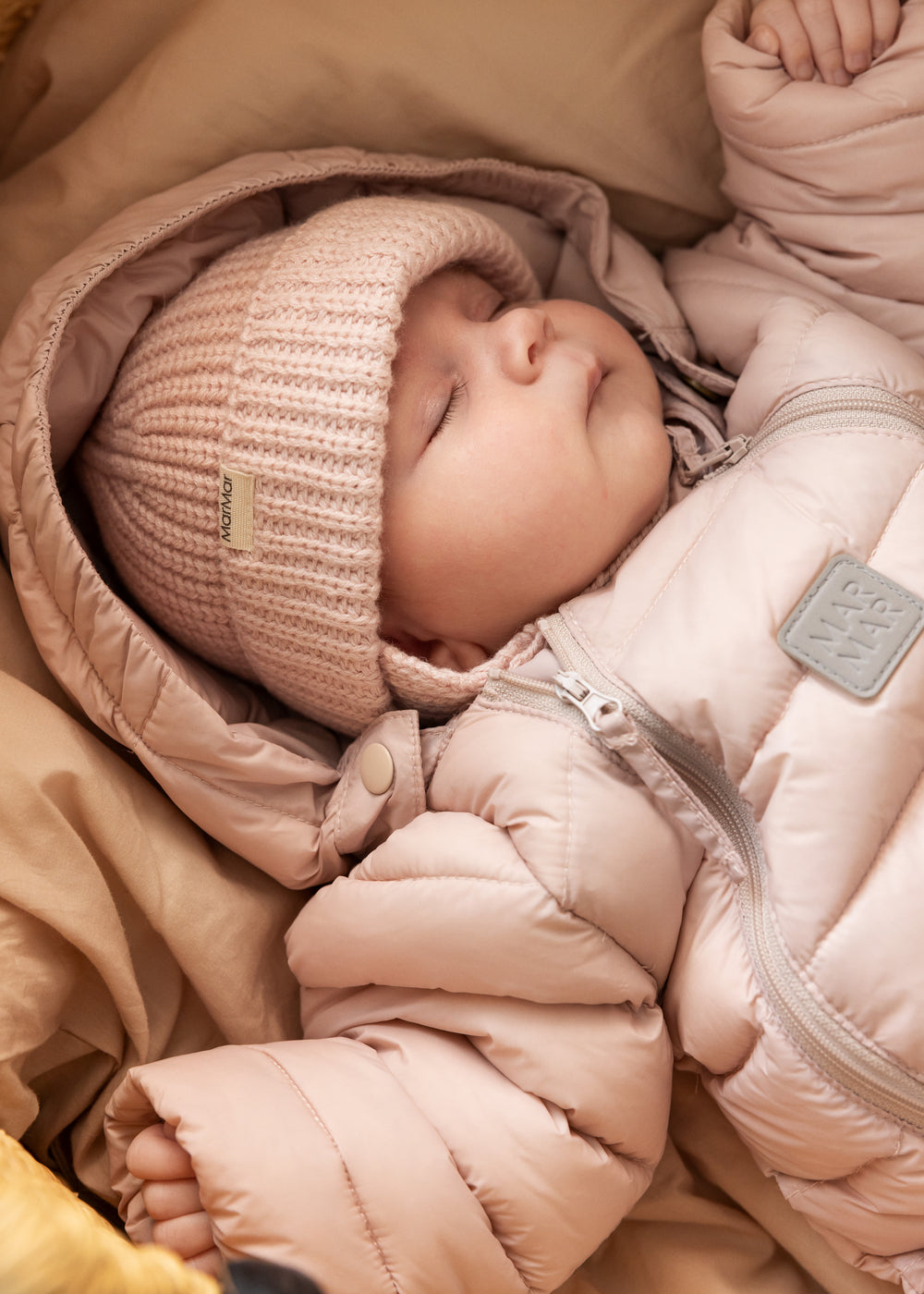 Baby iført lyserød dundragt og strikket hat