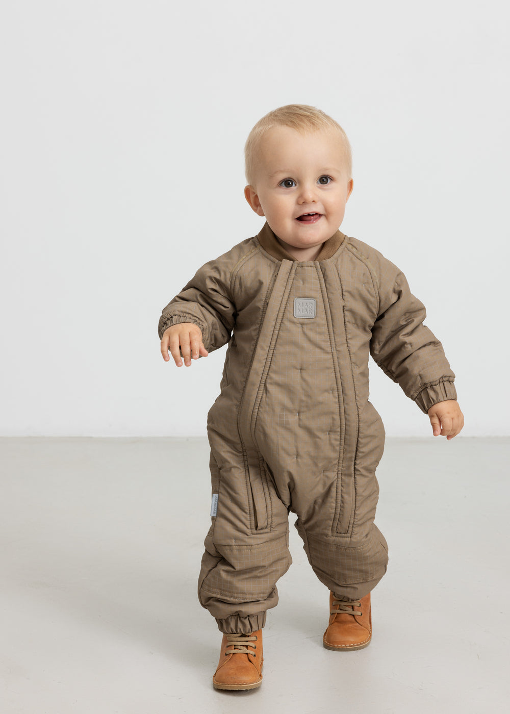 Baby iført brunternet termodragt, går mod kameraet