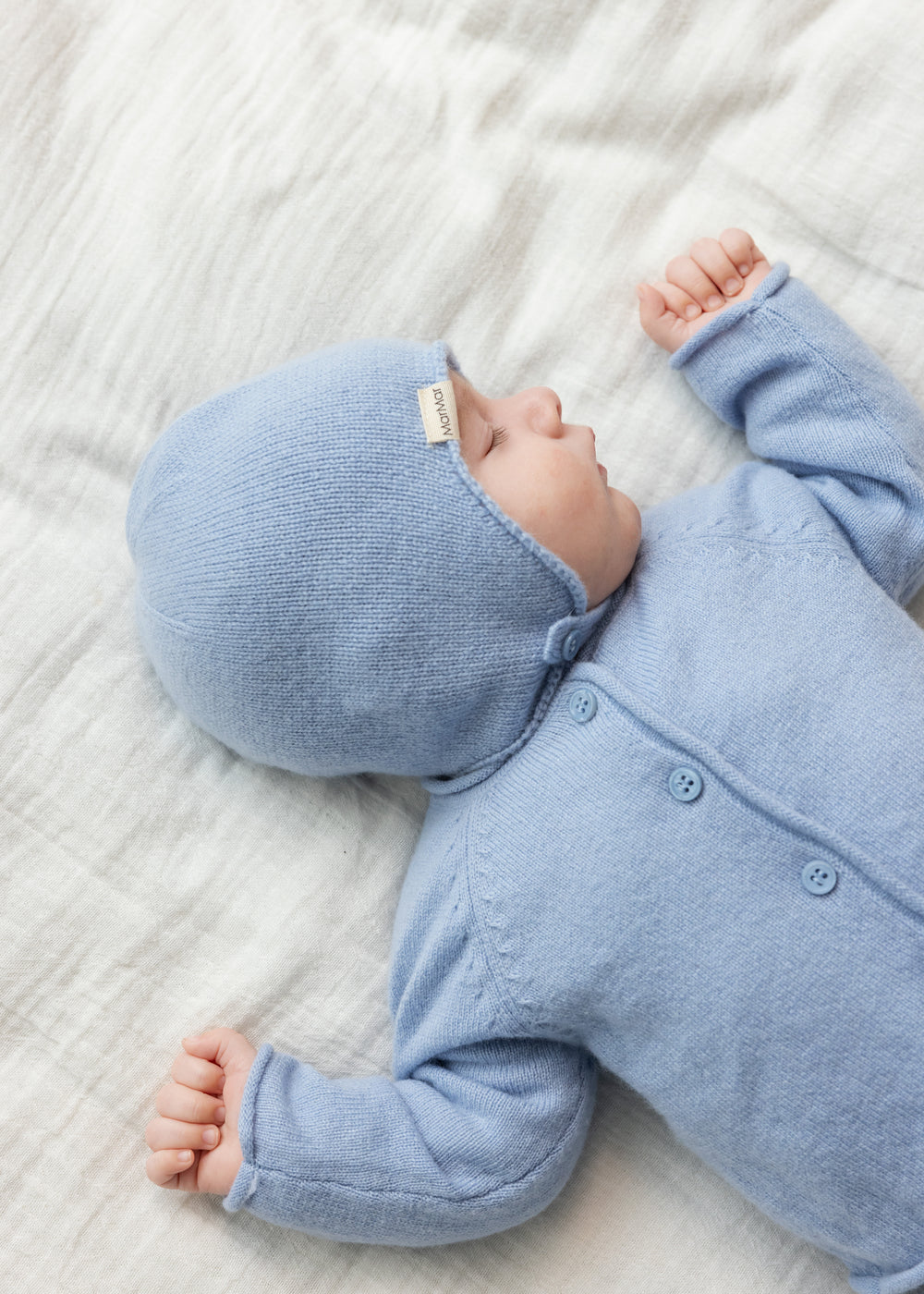 Lyseblå cardigan på baby med knaplukning og lange ærmer, synlige knapper foran