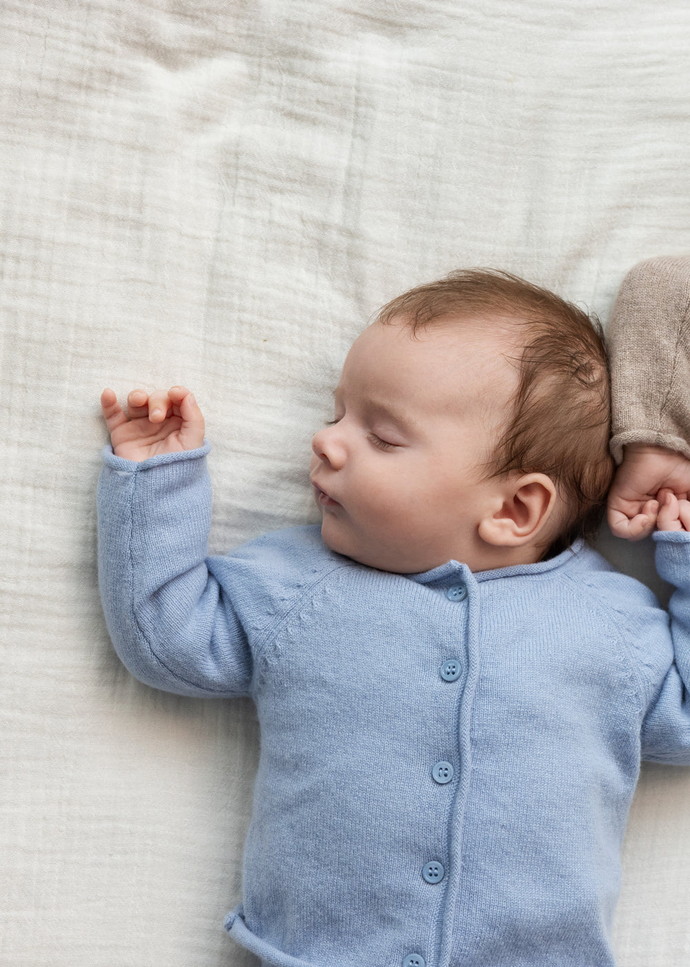Lyseblå cardigan med knaplukning på baby, rund hals og lange ærmer i bevægelse