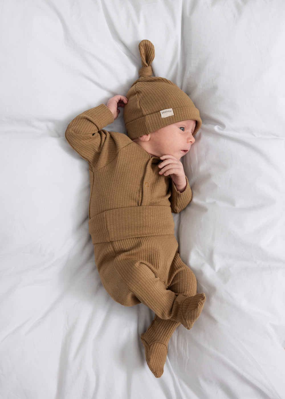 Baby med brune ribstrikkede babybukser med nedbukket kant og futter, babybody og babyhue.