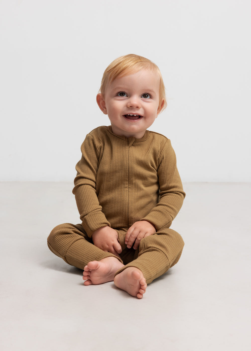 Baby iført ribbstrikket brun holdragt i blødt materiale med lange ærmer og lange ben og lynlås