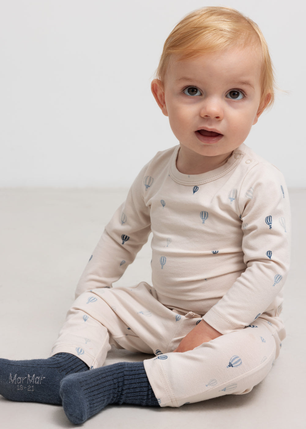 Beige bodystocking med luftballonprint i blå, lange ærmer, båret af lille barn.