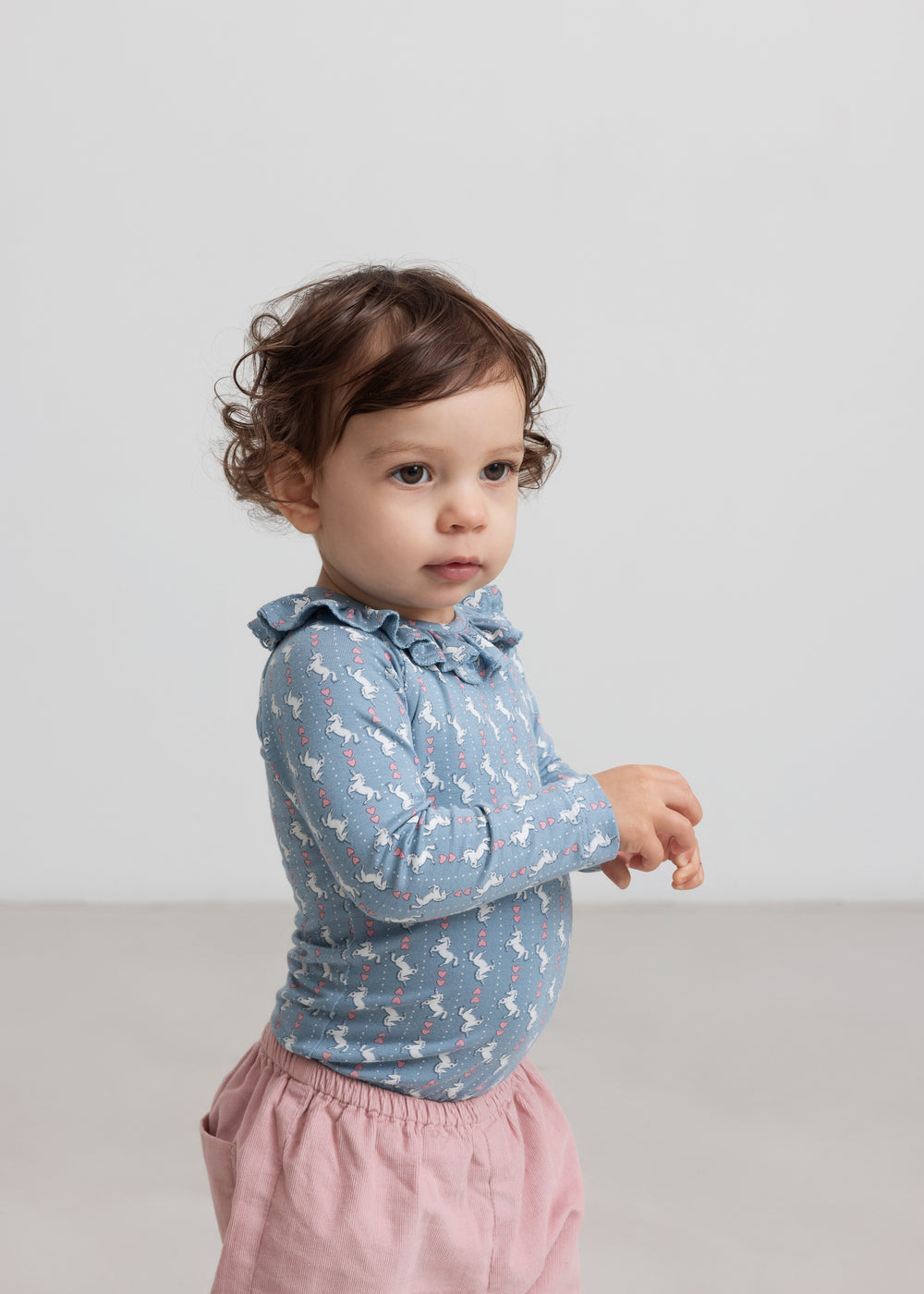 Baby iført blå body med enhjørningemønster og flæsekrave