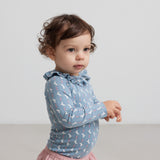 Baby iført blå body med enhjørningemønster og flæsekrave