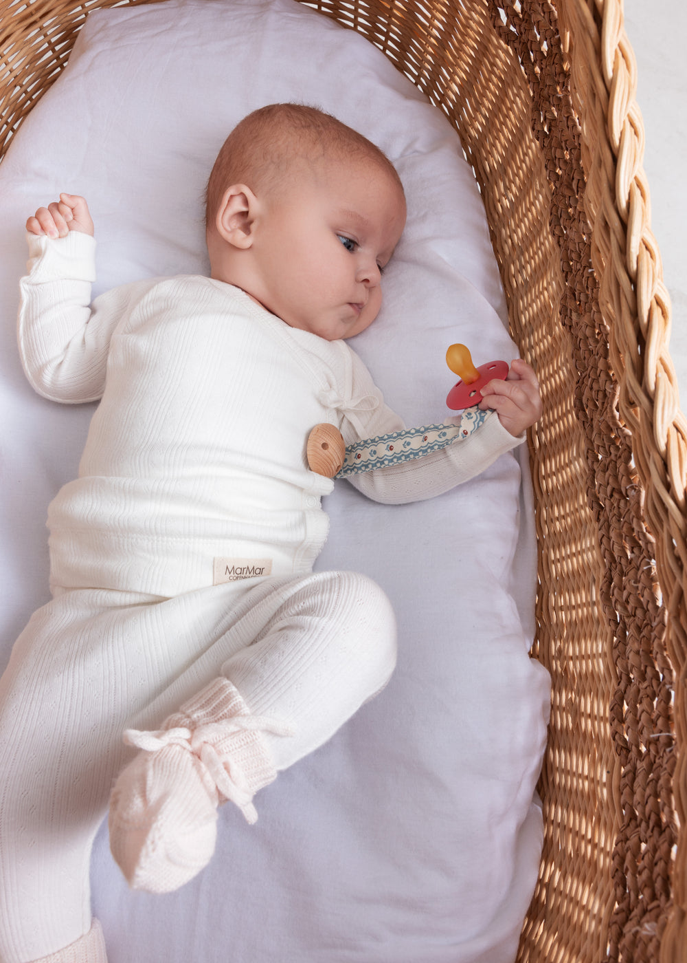 Baby med suttesnor og lille legetøj med træelement ved hånden