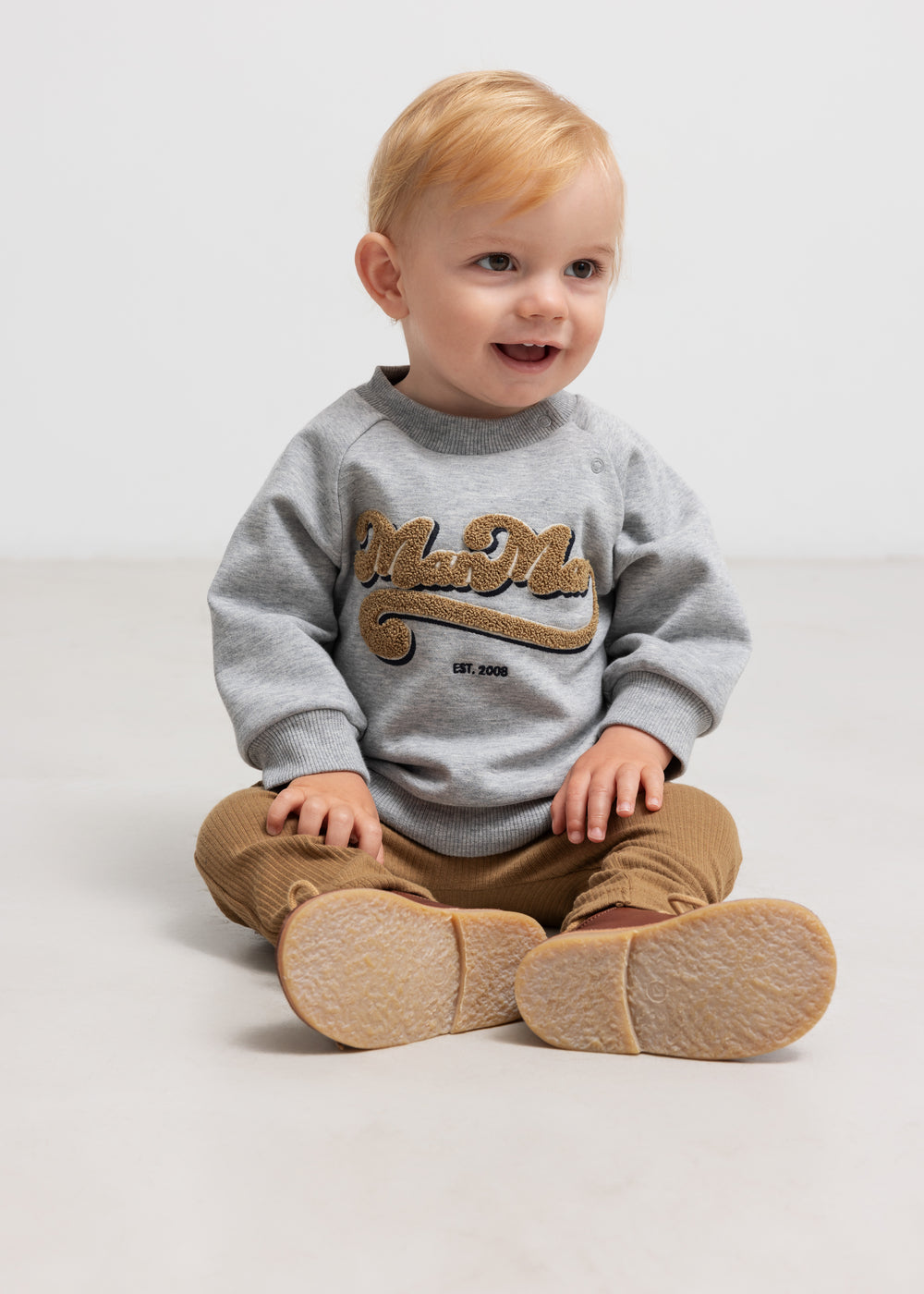Siddende barn i grå sweatshirt med guld broderi