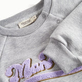 Nærbillede af broderi og ribkant på grå sweatshirt til børn