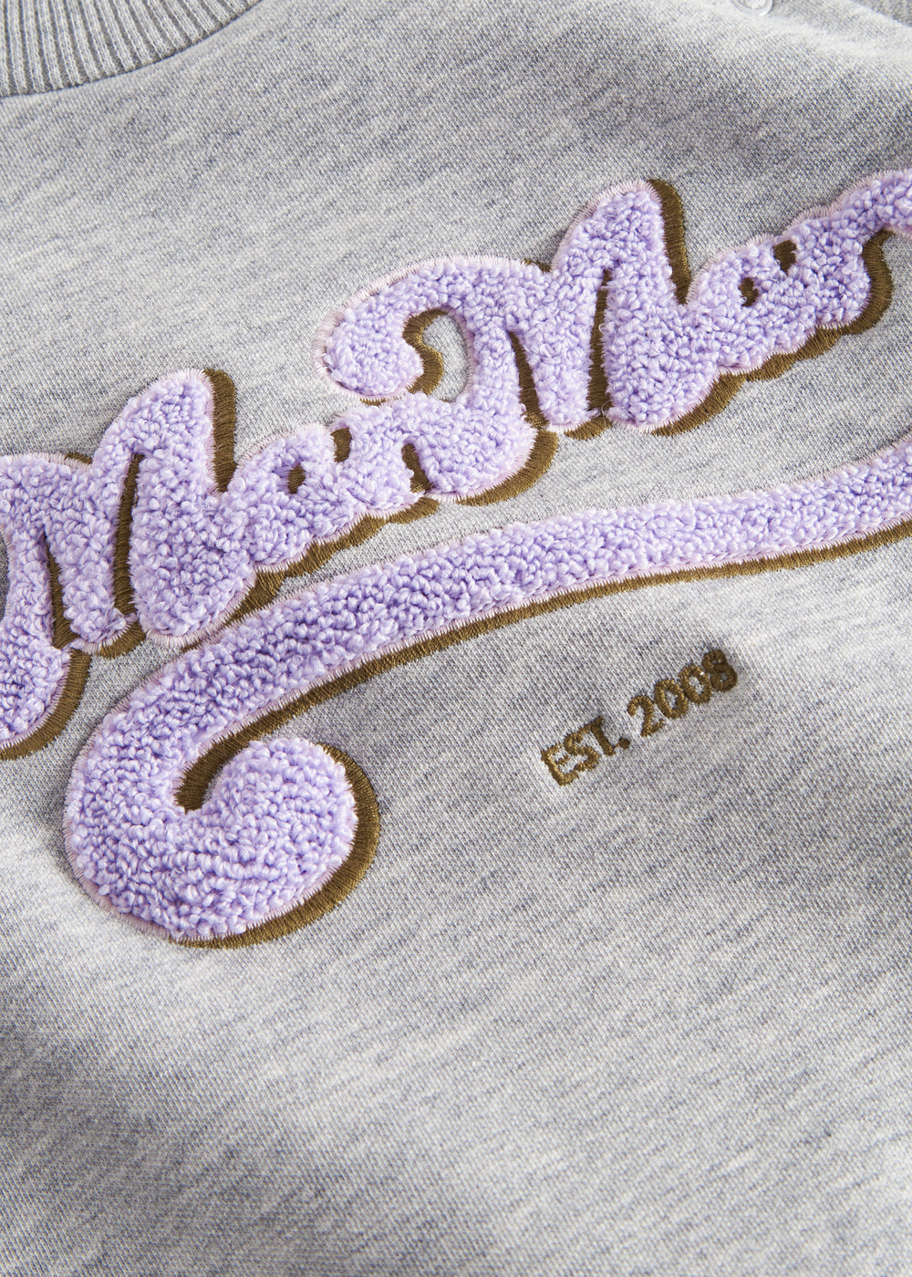 Detaljer af lilla og guld broderi på grå sweatshirt til børn