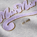 Detaljer af lilla og guld broderi på grå sweatshirt til børn