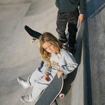 Børn med skateboard ved skatepark, iført grå sweatshirt og bukser