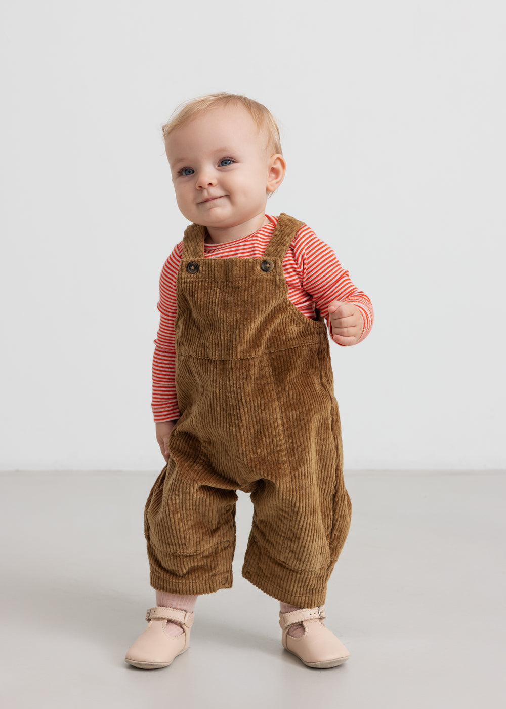 Baby iført brun fløjlsoverall og lyserød bluse