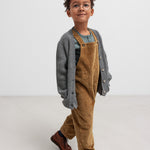 Dreng iført grøn ribstrikket bluse og brun overall.