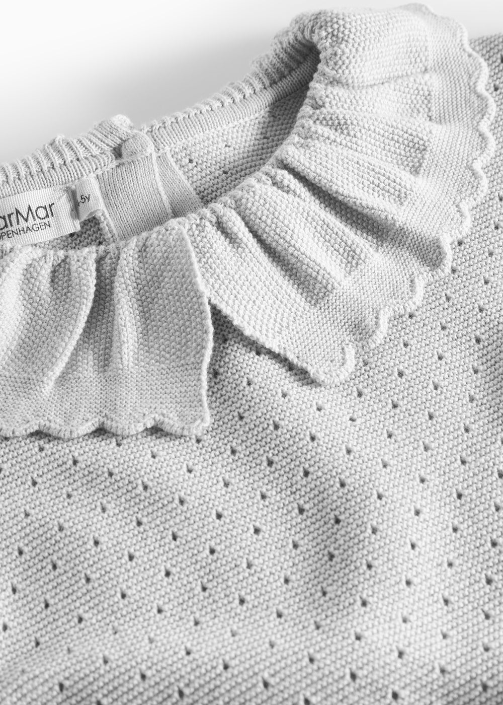 Detaljer af flæsekrave på grå strikbluse med hulmønster